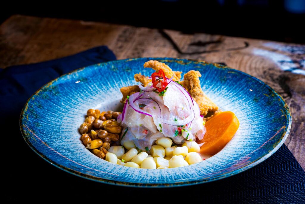 plato azul con comida que lleva cebolla roja, maíz, pescado crudo y camote