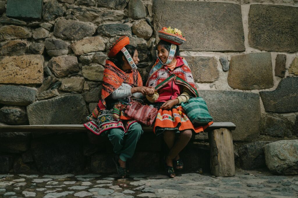 Dos mujeres Quechua hablando y sonriendo, con vestidos tradicionales, en la calle